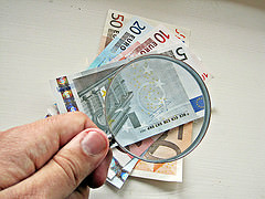 Hand Holding Magnifying Glass Examining Currency